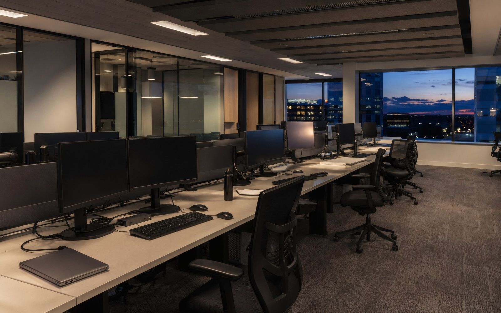 Office desks with monitors beside tall windows